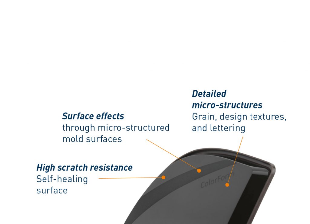 A close-up of a dark, curved object showcases features achieved through Injection Molding: micro-structured surfaces with surface effects, detailed grain and lettering, and a self-healing high scratch-resistant finish. White background, blue and orange text.